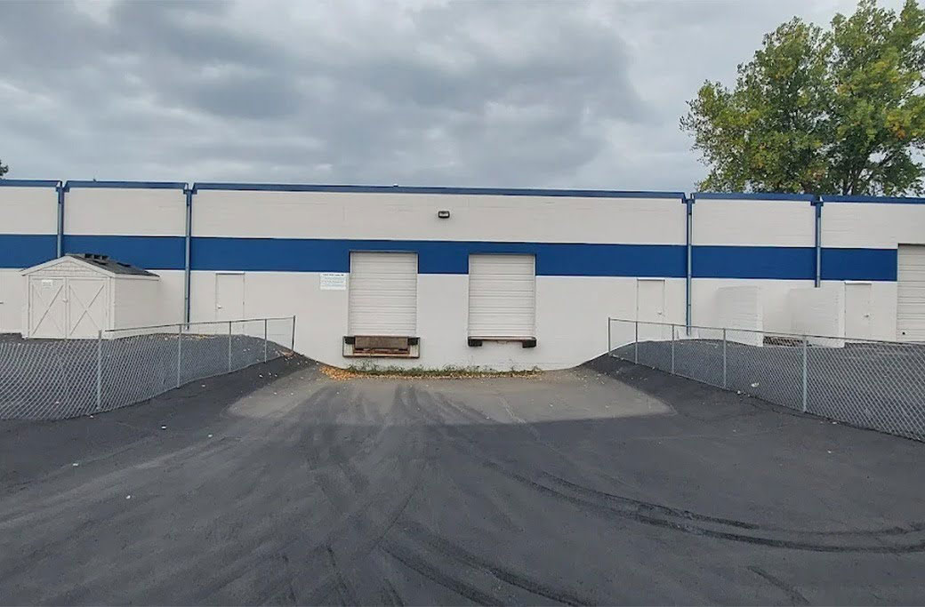 White commercial building with blue trim, overhead loading doors and fenced access ramps.
