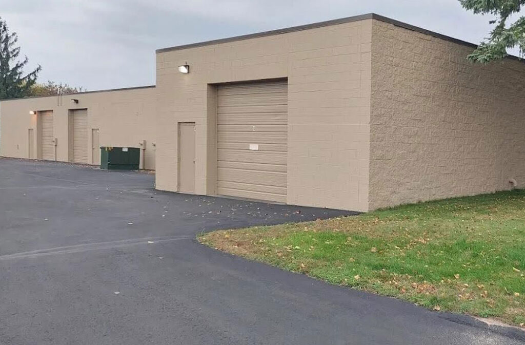 Tan commercial building with multiple overhead doors beside a paved access area.