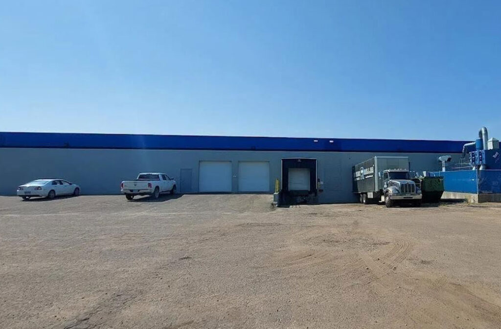 Gray commercial building with blue trim, overhead doors, a loading dock and parked trucks.